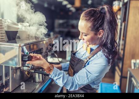 Die professionelle, gut gekleidete Barista dampft in einem Café von der Kaffeemaschine. Stockfoto