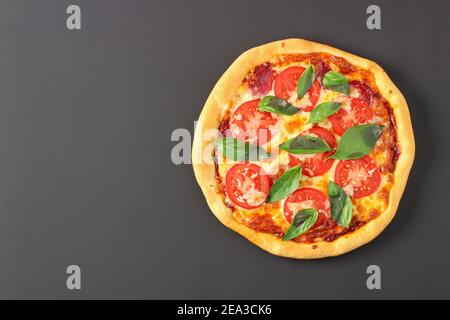 Pizza mit Käse, Wurst, Tomaten und Basilikumblättern isoliert auf schwarzem Hintergrund. Blick von oben Stockfoto