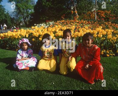 Großbritannien, England, London, Regents' Park, indische Mutter mit Kindern, die auf dem grünen Gras zwischen den gelben Tulpen sitzen. Stockfoto