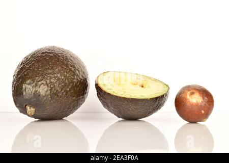 Eineinhalb ganze, dunkelgrün, reif duftend leckere Avocados, daneben ein ganzer brauner Stein aus der Avocado. Der Hintergrund ist weiß. Stockfoto