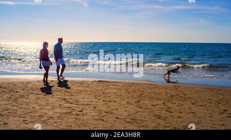 Marbella, Malaga, Spanien. Oktober 2020. Touristisches Paar, das mit seinem Hund an einem sonnigen Herbsttag an einem Strand in Marbella spazieren geht. Stockfoto