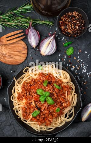 Pasta mit Hackfleisch und Tomatensauce bestreut mit Basilikum auf schwarzem Betonboden. Stockfoto
