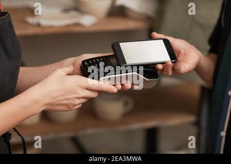 Warm getönte Nahaufnahme des Kunden zahlen über Smartphone mit leerem Bildschirm in Töpferei, Kopierraum Stockfoto