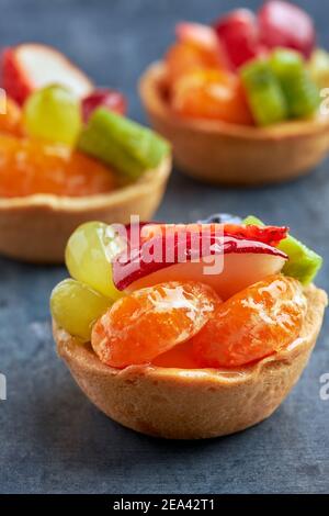 Set von Mini-Premium-Süßspeisen mit frischem Obst auf einem Biskuitboden auf einem Holztisch. Stockfoto
