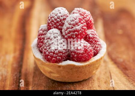 Appetitliche Himbeer-Torte mit Puderzucker auf einem Biskuitboden auf einem Holztisch. Stockfoto