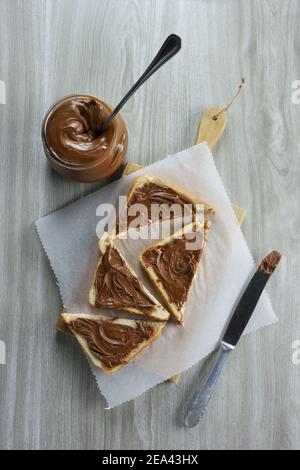 Brotscheibe mit Haselnuss-Praline-Paste auf einem Platte und graue Tabelle als Hintergrund Stockfoto