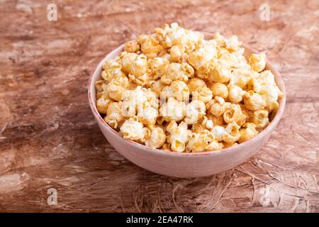 Popcorn mit Karamell in Keramikschale auf braunem Betongrund. Seitenansicht, Nahaufnahme. Stockfoto
