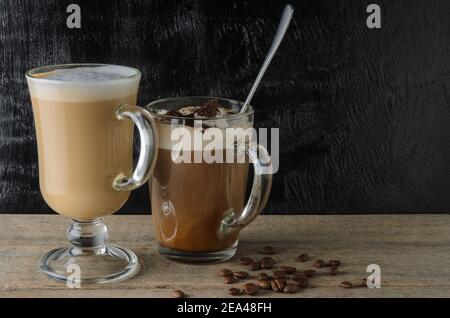 Zwei Glasplatten mit Cappuccino und Eisschokolade auf einem Holztisch mit schwarzem Strukturhintergrund. Selektiver Fokus. Stockfoto