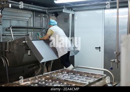 Rückansicht bei reifen Arbeiterinnen, die in der Werkstatt in der industriellen Lebensmittelfabrik Betriebsmittel betreiben, Kopierraum Stockfoto