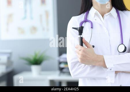 Arzt in Schutzmaske hält ein Otoskop in den Händen Stockfoto