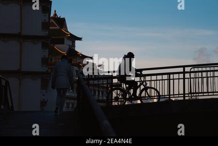 Silhouette des Mannes mit schützenden Anti-covid Maske auf seinem Kinn Reiten auf Brücke über Marne Fluss in Pariser Vorort. Frankreich. Stockfoto