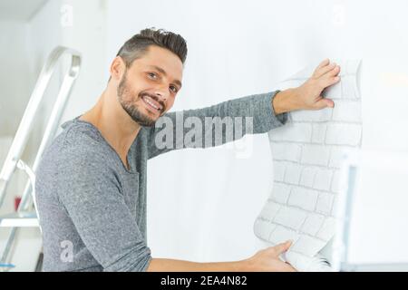 Mann hält Tapetenmuster an der Wand Stockfoto