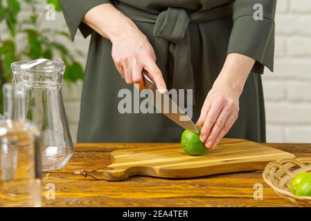 Frau schneiden Limette in der Küche, Zitronenwasser, erfrischendes Wasser mit Limette und Zitrone, gesunde Ernährung Konzept Stockfoto