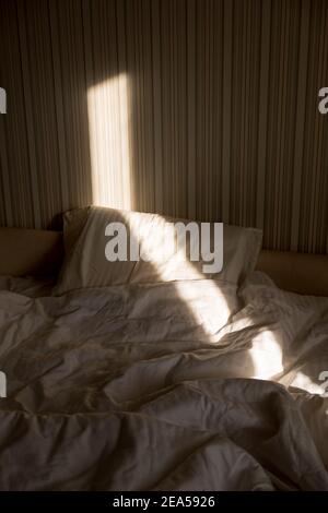 Sonnenstrahl fällt auf das Bett. Die Sonne strahlt am Morgen durch das Fenster. Neuer Tag mit warmem Sonnenlicht Flare. Stockfoto