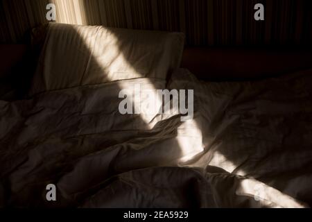 Sonnenstrahl fällt auf das Bett. Die Sonne strahlt am Morgen durch das Fenster. Neuer Tag mit warmem Sonnenlicht Flare. Stockfoto