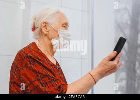 Eine ältere Frau in einer medizinischen Schutzmaske spricht vorbei Videoanruf auf einem Smartphone Stockfoto
