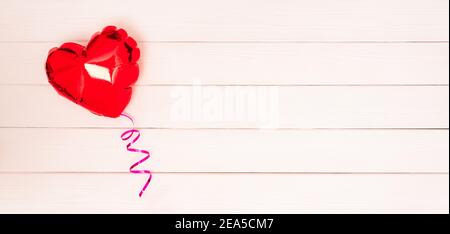 Ein roter Folienballon in Form eines Herzens mit einem rosa Band auf einem weißen beigen und rosa Holz Valentinstag Hintergrund Banner. Valentinstag Verbot Stockfoto