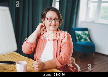 Erwachsene charmante Brünette Frau in Brille plus Größe Körper positiv Mit einer Tasse Tee zu Hause Stockfoto