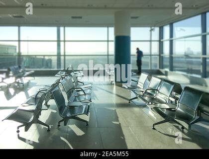 Fast leeres Flughafenterminal. Ein verschwommener Mann im Hintergrund. Covid-19 Reisebeschränkungen und Quarantäneisolation Konzept. Stockfoto