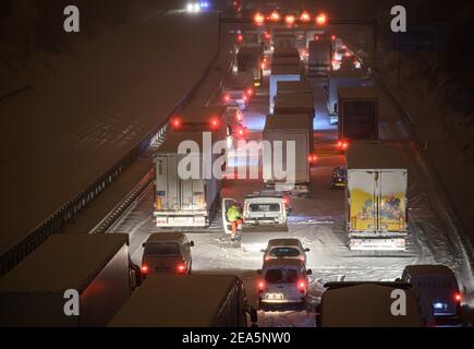 Dresden, Deutschland. Februar 2021, 08th. Auf der verschneiten Autobahn 4 bei Dresden stecken Autos und Lastwagen im frühen Schneefall in einem Stau fest, während ein Mann neben seinem Auto steht. Quelle: Robert Michael/dpa-Zentralbild/dpa/Alamy Live News Stockfoto