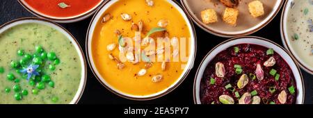 Veganes Suppenpanorama. Eine Auswahl von Gemüsesuppen, von oben geschossen, eine flache lag auf einem schwarzen Hintergrund Stockfoto