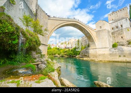 Ein kleiner Wasserfall an der Unterseite der Brücke von Mostar in Bosnien und Herzegowina als Touristen genießen den Blick auf das smaragdgrüne Wasser des Flusses Neretva Stockfoto