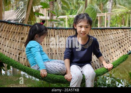 Zwei nette junge asiatische Mädchen, die zusammen auf einer Bambuswoben Hängematte ruhen, Spaß haben und entspannen. Stockfoto