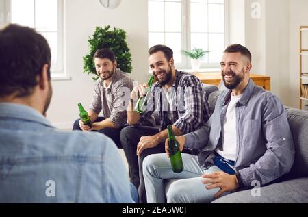 Gruppe von glücklichen Freunden sitzen auf dem Sofa im Wohnzimmer, trinken Bier und reden Stockfoto