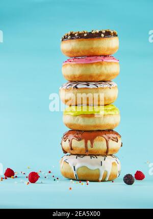 Bunte Donuts mit Glasur und Streuseln in einem Stapel auf blauem Hintergrund gestapelt. Stockfoto
