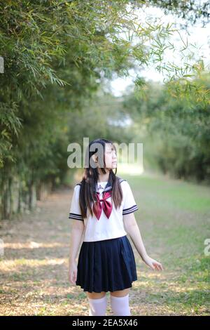 Portrait von schönen asiatischen japanischen High School Mädchen Uniform suchen Mit Bambus Wald Hintergrund Stockfoto