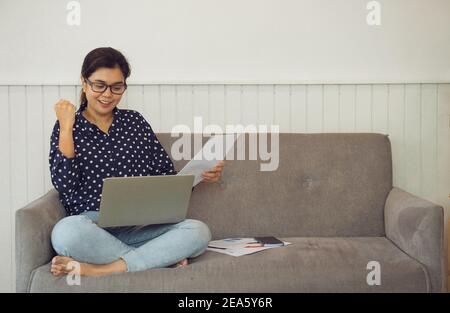 Business-Frau hält Papierkram und Video-Anrufe über Laptop sprechen Sie mit Assistant in Home.She ist sehr glücklich, den Auftrag auf einem Video-Meeting zu bekommen. Arbeitsfr Stockfoto