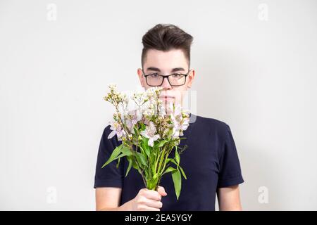 Serious junger Mann in Gläsern mit einem Bouquet von Weiß Blumen auf grauem Hintergrund Stockfoto