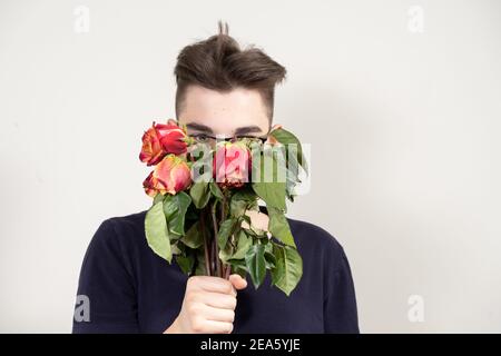 Junger Mann in Gläsern mit einem Strauß verdorrte rote Rosen. Unglückliche Liebe Konzept Stockfoto