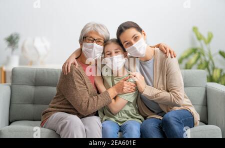 Ein nettes Mädchen, ihre Mutter und Großmutter genießen es, Zeit zusammen zu Hause zu verbringen. Menschen mit Gesichtsmasken. Stockfoto