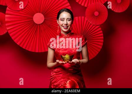 Schöne lächelnde asiatische Frau mit alten chinesischen Goldbarren vertreten Wohlhabende in roten orientalischen Stil Hintergrund für das chinesische neue Jahr Konzepte Stockfoto