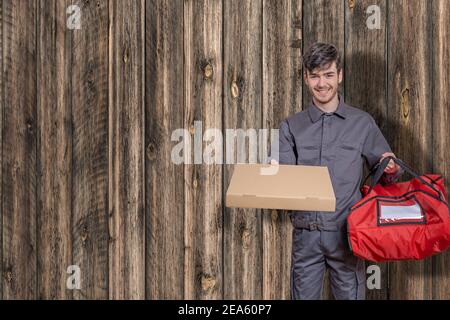 Fast-Food-Delivery-Mann mit Pizza-Boxen in den Händen liefern die Bestellung für die Lieferung, in Uniform gekleidet und lächelnd, mit roten Beutel Stockfoto