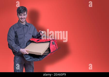 Fast-Food-Delivery-Mann mit Pizza-Boxen in den Händen liefern die Bestellung für die Lieferung, in Uniform gekleidet und lächelnd, mit roten Beutel Stockfoto