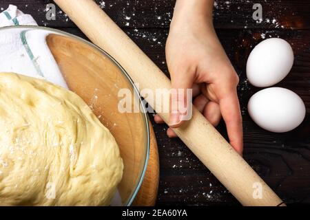 Nudelholz zum Rollen des Teigs in weiblichen Händen. Hefeteig kochen. Teig zum Backen von Brot in einer Glasschüssel. Stockfoto