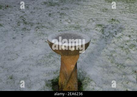 Gefrorenes Wasser in einem Stone Bird Bad umgeben von Schnee in einem Country Cottage Garden in Rural Devon, England, Großbritannien Stockfoto
