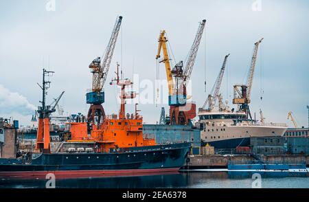 Blick auf den Seehafen mit Portalkranen und Liegeplätzen für Frachtschiffe. Kräne im Frachthafen von St. Petersburg in der Winterzeit Stockfoto