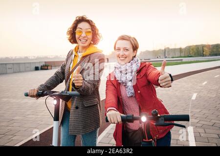 Zwei Freundinnen fahren moderne gemietete Elektroroller durch die Straßen der Stadt. Transport und Lifestyle und Freundschaftskonzept Stockfoto