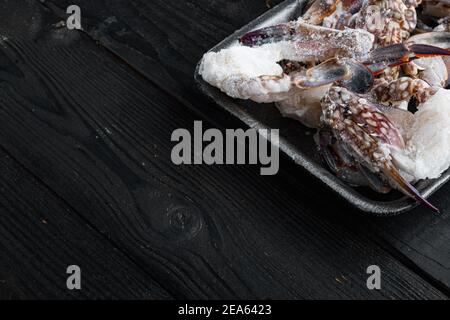 Frische rohe Blume Krabbe oder blaue Krabbe gefrorene Teile Set, in Kunststoff-Tablett, auf schwarzem Holztisch Hintergrund, mit Copyspace und Platz für Text Stockfoto