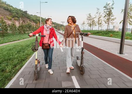 Zwei Freundinnen fahren moderne gemietete Elektroroller durch die Straßen der Stadt. Transport und Lifestyle und Freundschaftskonzept Stockfoto