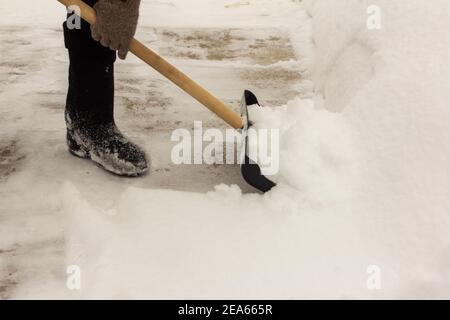 Ein Mann in Filzstiefeln, mit einer Schaufel in den Händen, entfernt nach einem Schneefall Schnee vom Bürgersteig. Stockfoto