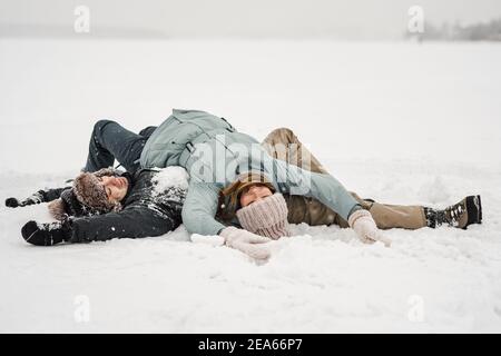 Liebevoller Kerl und Mädchen liegen im Schnee. Junge glückliches Paar zu Fuß im Wintertag Stockfoto