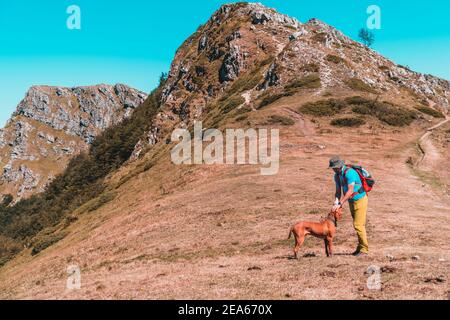 Der junge Tourist und sein Hund ruhen sich aus und spielen zusammen Auf dem Gipfel des Berges Stockfoto