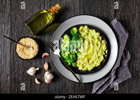 Brokkoli Kartoffelbrei bestreut mit gehackten Mandeln serviert mit gedünsteten Brokkoli-Röschen auf einem schwarzen Teller auf einem dunklen Holztisch, horizontale Ansicht von Stockfoto