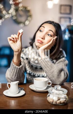 Traurige Frau in einem Café, die träumerisch auf ein Stück weißen Zucker für ihren Kaffee schaut. Sagen Sie Nein zu Zucker und schnelle Kohlenhydrate. Diät für Diabetes und sucht zu schwitzen Stockfoto