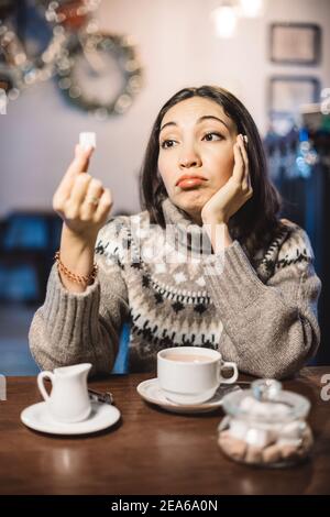 Traurige Frau in einem Café, die träumerisch auf ein Stück weißen Zucker für ihren Kaffee schaut. Sagen Sie Nein zu Zucker und schnelle Kohlenhydrate. Diät für Diabetes und sucht zu schwitzen Stockfoto