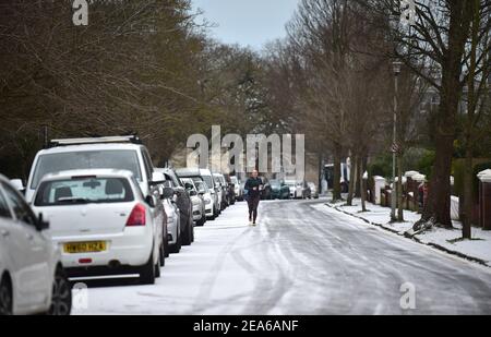 Brighton UK 8th February 2021 - EIN Läufer stampft die verschneiten Straßen rund um den Queens Park in Brighton nach einem leichten Schneefall über Nacht mit weiteren Prognosen für Teile des Ostens und Südostens heute: Credit Simon Dack / Alamy Live News Stockfoto